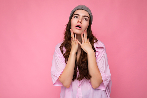 Attractive fatigue exhausted young curly brunette woman wearing pink shirt and gray hat isolated on pink background with copy space.