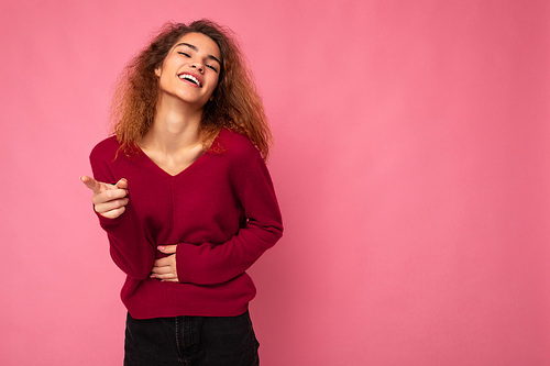 Photo of young european happy joyful laughing positive charming cute brunette curly woman with sincere emotions wearing trendy pink sweater isolated over pink background with free space.
