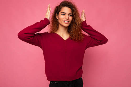 Portrait of young joyful happy positive smiling beautiful brunette curly woman with sincere emotions wearing trendy pink pullover isolated on pink background with copy space and having fun.