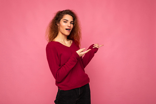 Photo of young happy positive amazed beautiful brunette wavy woman with sincere emotions wearing casual pink jersey isolated over pink background with copy space and pointing at free space for text.