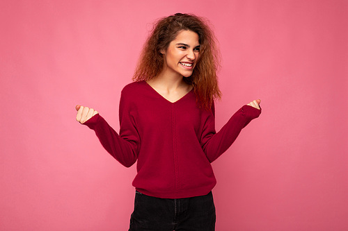 Photo of young emotional joyful happy smiling beautiful brunette curly woman with sincere emotions wearing casual pink pullover isolated over pink background with copy space and saying yeah.