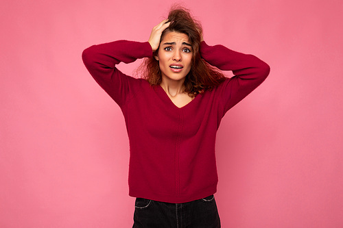Portrait of young emotional amazed shocked beautiful brunette curly woman with sincere emotions wearing trendy pink pullover isolated on pink background with copy space.