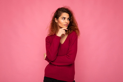 Photo of young european thoughtful charming cute brunette curly woman with sincere emotions wearing trendy pink sweater isolated over pink background with free space.