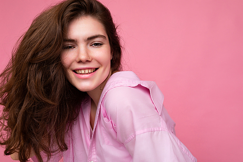 Portrait of beautiful positive cheerful cute smiling young brunette woman in stylish shirt isolated on pink background with copy space.