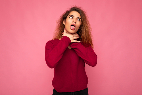 Portrait of young emotional beautiful brunette curly woman with sincere emotions wearing trendy pink pullover isolated on pink background with copy space and showing strangle and chocke.