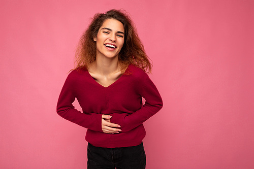 Photo of young delightful happy positive charming brunet wavy woman with sincere emotions wearing casual pink pullover isolated over pink background with empty space and laughing.