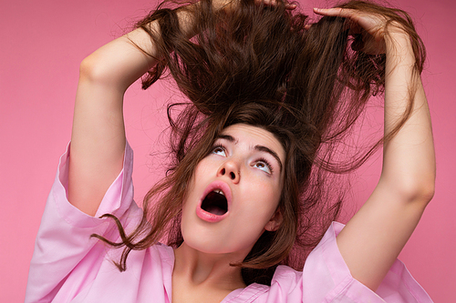 Beautiful shocked amazed young curly brunette woman wearing pink shirt and grey hat isolated on pink background with copy space.