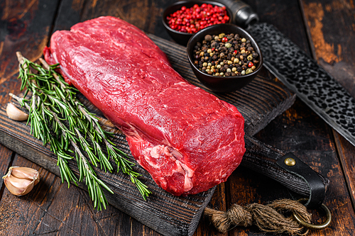 Whole Raw Tenderloin veal meat for steaks fillet mignon on a wooden cutting board with butcher knife. Dark  wooden background. Top view.