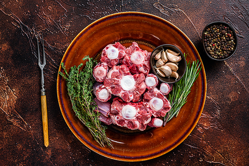 Fresh uncooked beef Oxtail cut Meat on rustic plate with herbs. Dark background. Top view.