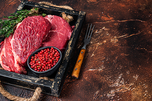 Fresh Raw Chuck eye roll beef steak in a wooden tray with herbs. Dark background. Top view. Copy space.