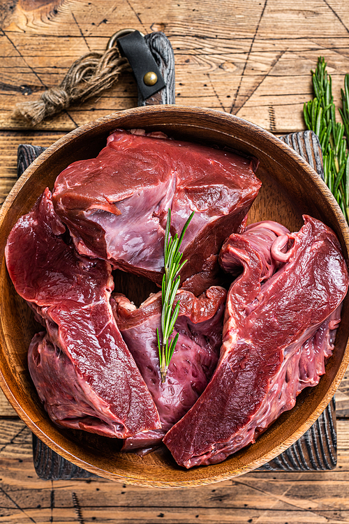 Sliced Beef or veal raw heart in a wooden plate with herbs. wooden background. Top View.