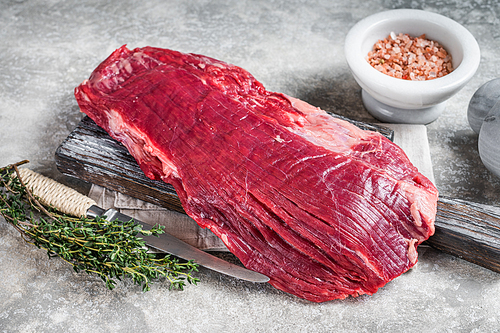Fresh Flank or flap raw beef steak on wooden board with herbs. Gray background. Top view.