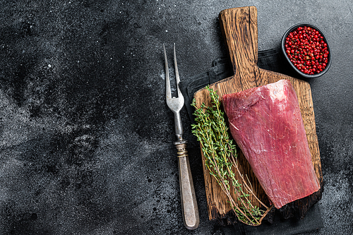 Raw Beef Tenderloin fillet meat on butcher wooden board. Black background. Top view. Copy space.