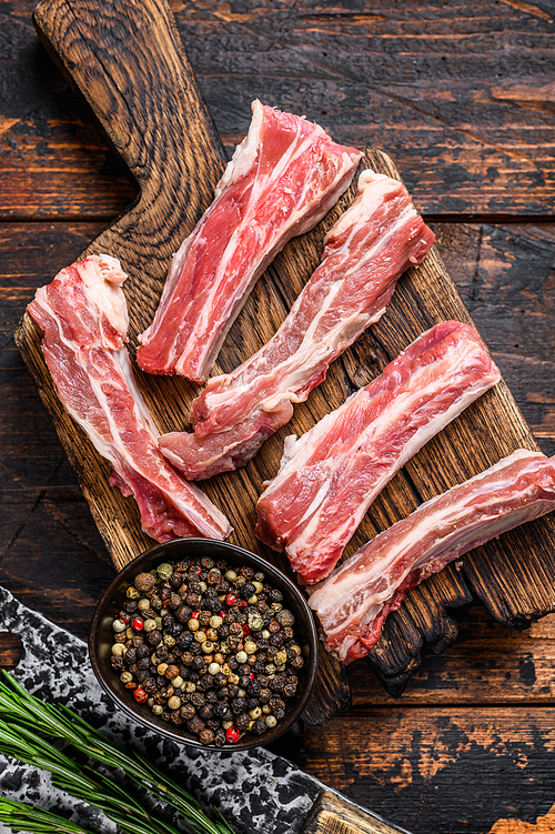 Raw sliced veal short spare loin ribs on a wooden cutting board. Black background. Top view.