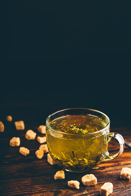 Cup of green tea with brown tea sugar on a wooden background
