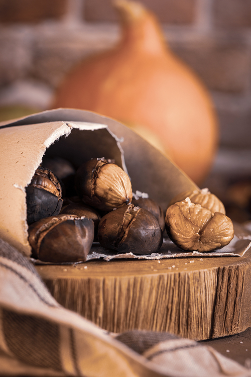 Roasted chestnuts in a paper cone, on a rustic kitchen countertop.