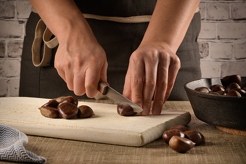 Woman cuts chestnuts on wooden cutting board.