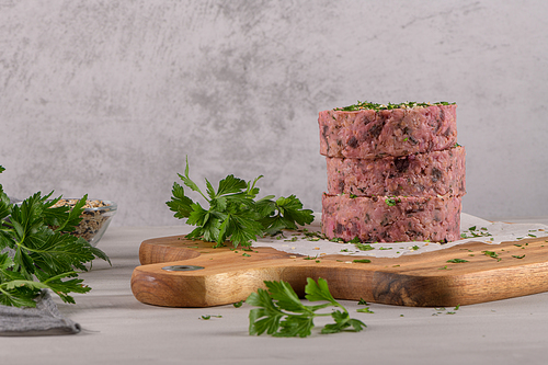 Raw veggie burger with beetroot and white beans with parsley leaves on wood cutting board.