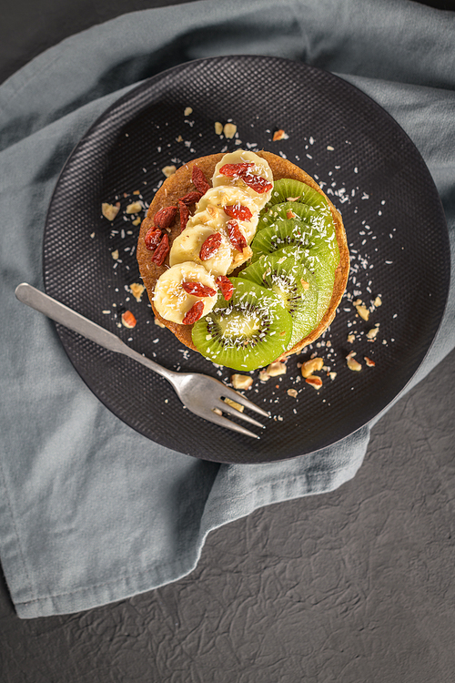 Healthy breakfast table,  homemade pancakes with kiwi, banana, goji and walnuts.