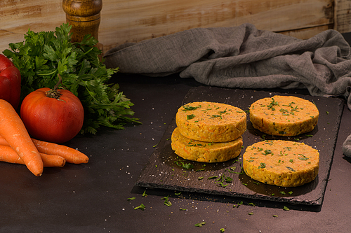 Raw veggie burger with chickpeas, vegetables and parsley leaves on kitchen countertop.