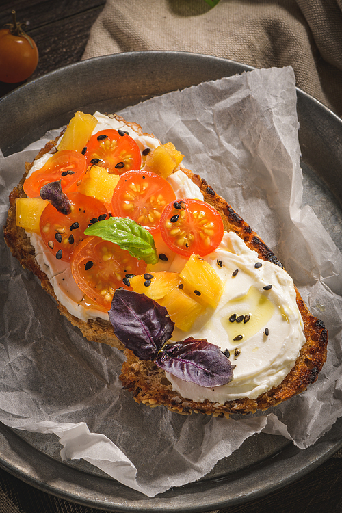 Italian bruschetta with roasted tomatoes, mozzarella cheese, pineapple slices and herbs on a metal plate.