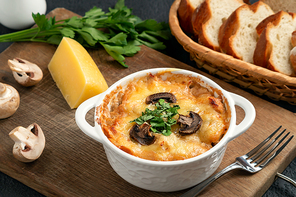 Casserole with chicken, mushrooms and cheese, known in Russia as julienne in white bowl with herbs on a wooden board, close up.