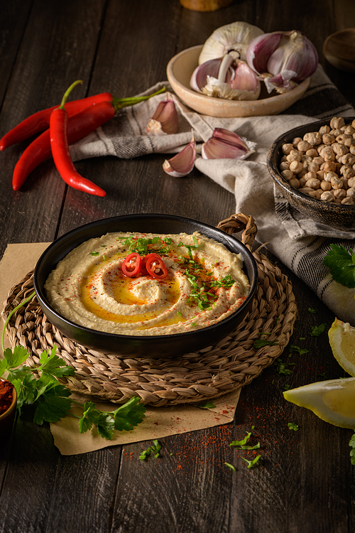 Delicious hummus in ceramic bowl. Colorful snack composition on a black wooden background.