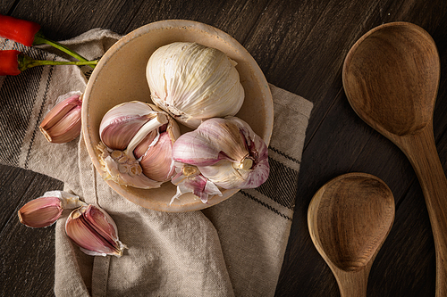Garlic on ceramic bowl and wooden spoons on a dark background. View from above.