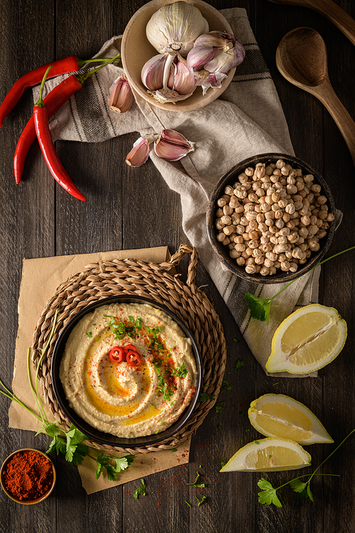 Delicious hummus in ceramic bowl. Colorful snack composition on a black wooden background.