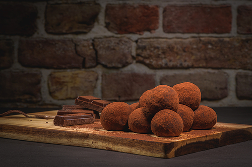 Craft chocolate truffles on wooden board with cocoa powder.