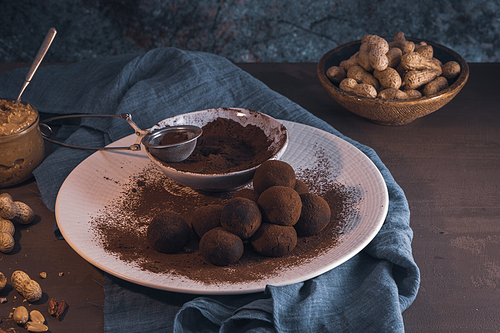 Craft chocolate truffles on plate with cocoa powder and peanuts.