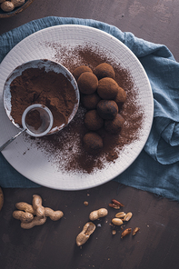 Craft chocolate truffles on plate with cocoa powder and peanuts.