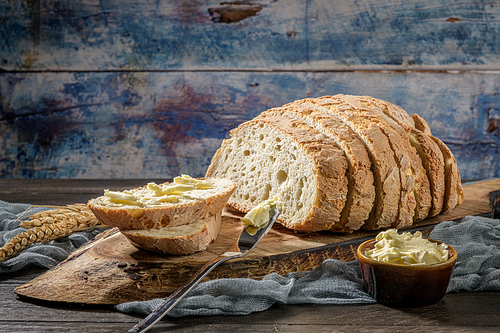 Buttered slice of freshly bake wheat bread with a butter knife on a rustic board.