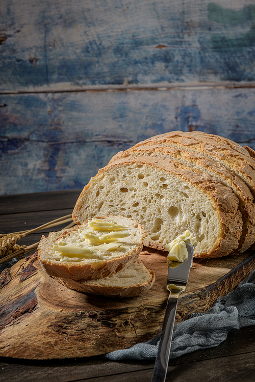 Buttered slice of freshly bake wheat bread with a butter knife on a rustic board.