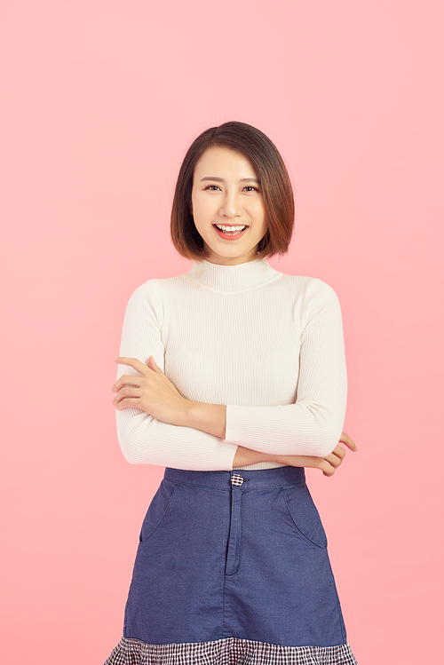 Smiling of Asian woman crossing her arms and standing isolated on pink background.