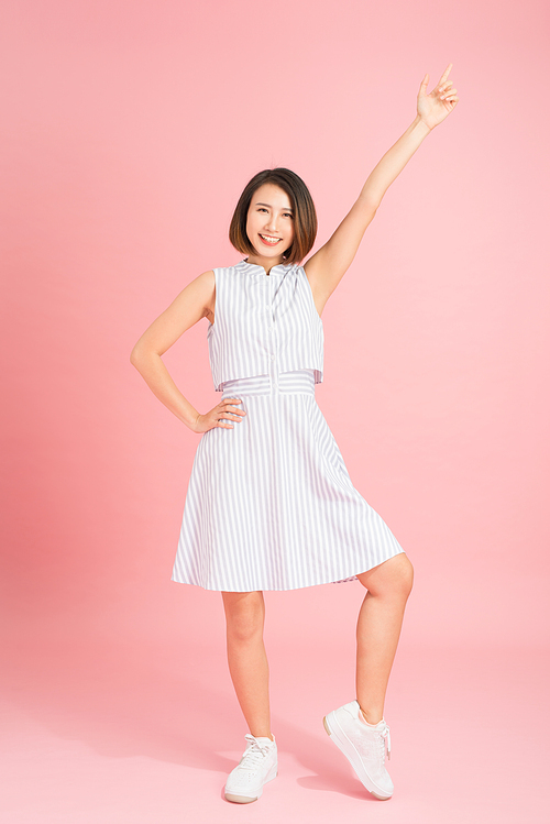 Beautiful young woman in light blue dress dancing on pink background