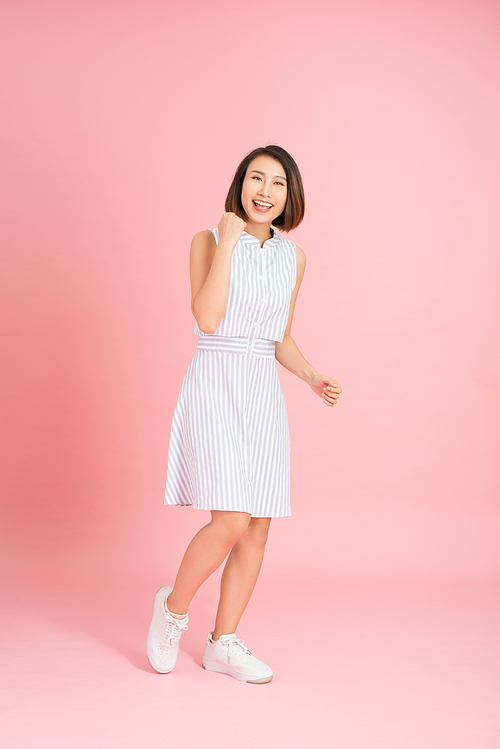 Full length portrait of happy exited pretty girl in elegant light blue dress  while jumping over pink background