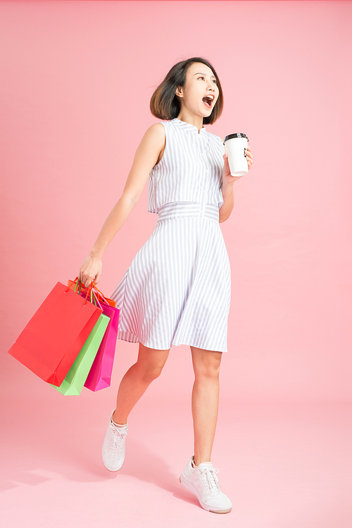 Woman carrying shopping bags enjoying cup of coffee concept isolated on pink with advertising area