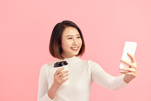 Young Asian woman selfie with her coffee cup on pink background.