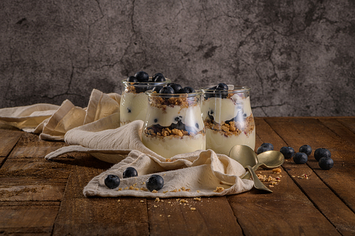 Yogurt parfait with blueberry and granola. Healthy breakfast concept served in mason jar with decorative spoons on wooden table.