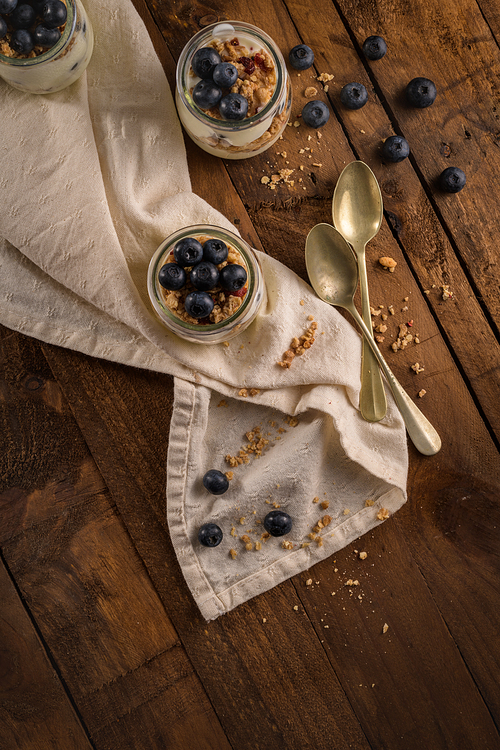 Yogurt parfait with blueberry and granola. Healthy breakfast concept served in mason jar with decorative spoons on wooden table.