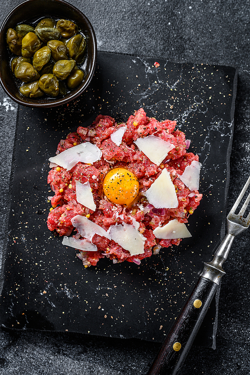 Tartar beef with a quail egg, capers and  Parmesan cheese. Black background. Top view.