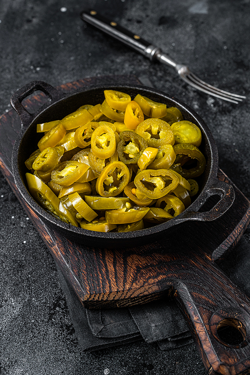 Pickled Green Sliced Jalapenos in a pan. Black background. Top view.