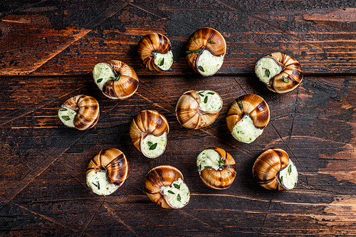 Snails with garlic butter in a wooden tray. Wooden background. Top view. Copy space.