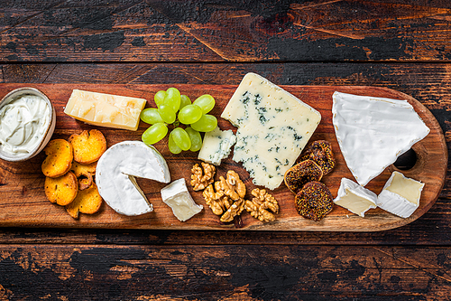Assorted Cheese board with Brie, Camembert, Roquefort, parmesan, blue cream cheese, grape and nuts. Dark wooden background. Top view.