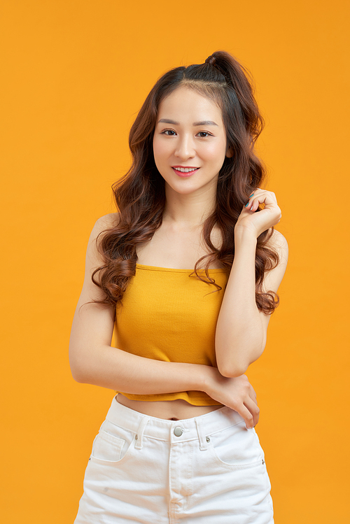 Joyful young asian woman in yellow crop top posing isolated on yellow background.