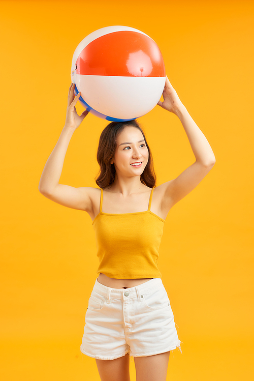 Casual beautiful Asian woman with beach accessories holding colorful ball in orange background