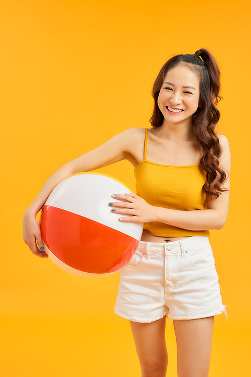 Happy young Asian woman holding beach ball in summer holiday travel on orange background.