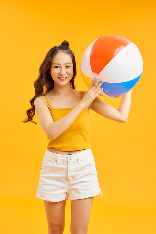 Happy young Asian woman holding beach ball in summer holiday travel on orange background.