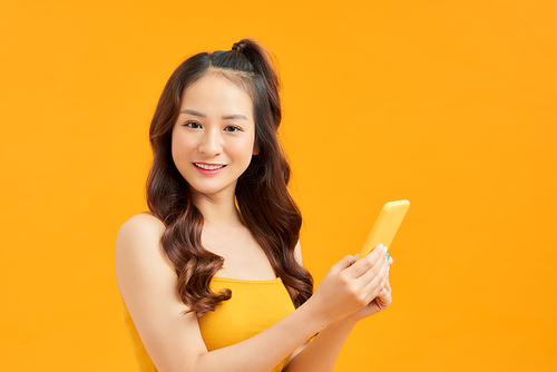 Attractive young Asian woman using phone over orange background.